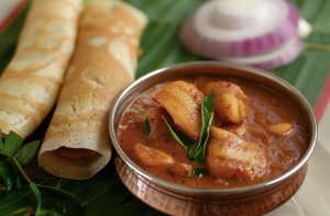Indian-style fish sambal served with dosa on a banana leaf with onion garnish. 