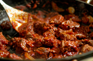 A cast iron pan sizzling with Mutton Ghee Roast, chunks of tender mutton pieces coated in spices and ghee.