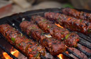 Mutton seekh kebabs being cooked on a skewer over a charcoal grill.