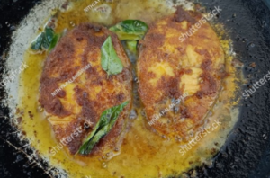 Surmai fish fillets sizzling in hot oil in a frying pan.