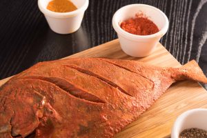 Marinated pomfret fish for fish tawa fry recipe on a wooden board with turmeric, chilli powder, and pepper powder around.