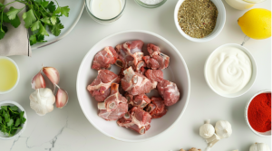 A plate of fresh mutton pieces surrounded by ingredients for preparing mutton biryani 