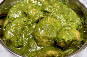 A bowl of marinated chicken skewers with vibrant green mint and coriander paste, ready to be grilled for Chicken Hariyali kabab.