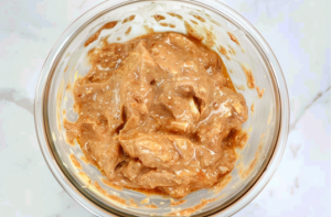 A bowl filled with marinated chicken pieces ready to be made into crispy chicken popcorn..