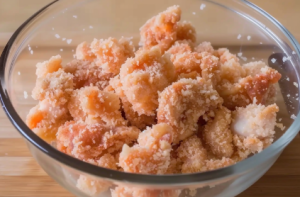 A bowl of marinated chicken pieces coated in golden breadcrumbs, ready to be fried into crispy chicken popcorn.