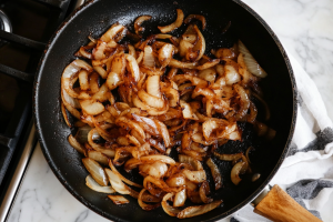 A pan filled with golden-brown onions frying in hot oil, sizzling and turning crisp for Nadan Kozhi Curry recipe